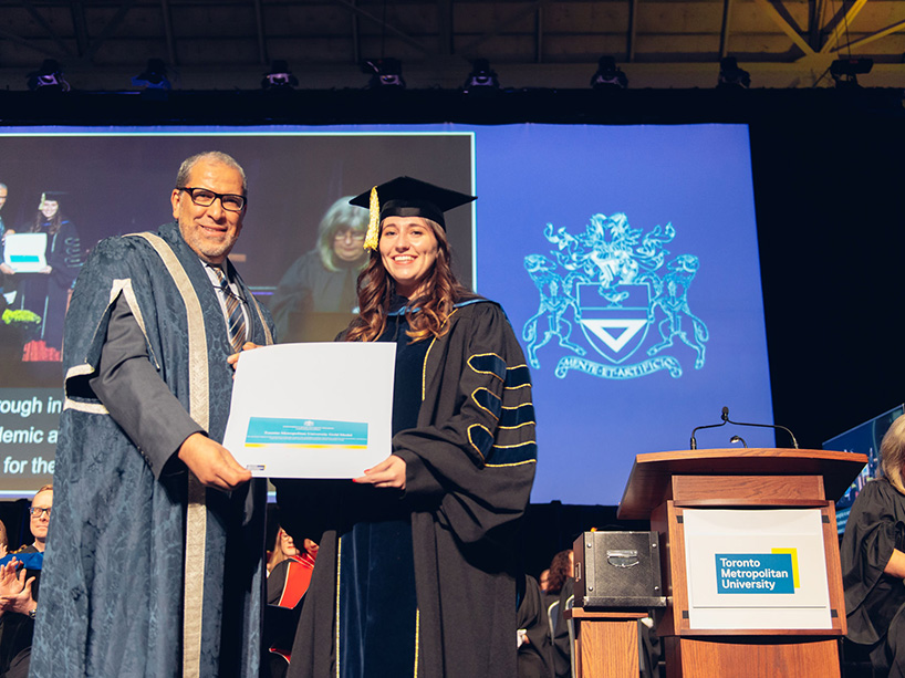 Bev Fredbord is pictured holding her gold medal certificate at the Fall 2022 convocation ceremony, standing next to President Mohamed Lachemi.