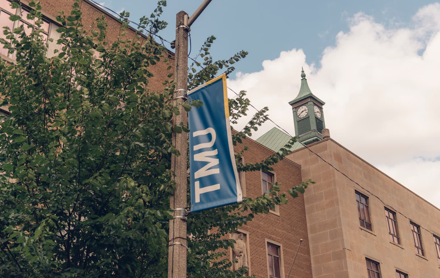 TMU street flag in front of a campus building against a backdrop of blue sky.